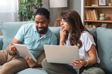 Evde dizüstü bilgisayarda ve yeni projede dijital tablette çalışan genç çift. Yenilikçi teknoloji uzmanları çevrimiçi çalışmalarla finans ve ekonomi krizine çözüm buldular.