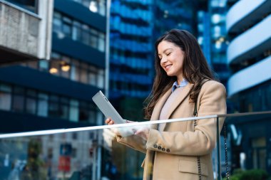 İş yerinin önünde dikilirken dijital tablet kullanan başarılı bir iş kadını. Genç iş adamı, profesyonel iş adamı, şehir sokaklarında modern teknoloji geliştiricisi..