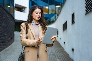 İş yerinin önünde dikilirken dijital tablet kullanan başarılı bir iş kadını. Genç iş adamı, profesyonel iş adamı, şehir sokaklarında modern teknoloji geliştiricisi..