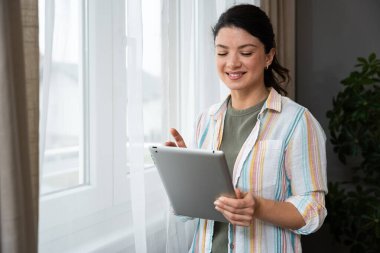 Ev ofisinde dijital tablet üzerinde çalışan çekici bir kadın. İş kadını küçük bir şirket sahibi dairesinden internet üzerinden çalışıyor. Bağımsız serbest grafik tasarımcı kadın özgürlük ve işin tadını çıkarıyor.