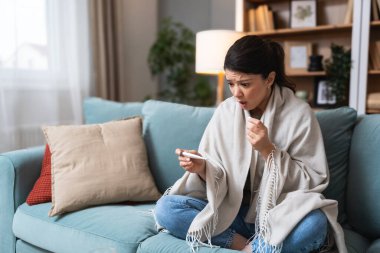 Hastalık mevsimsel virüs problemi konsepti. Kanepede elinde termometreyle yatan hasta bir kadın. Hasta kadın yüksek ateşle yatakta yatıyor. Soğuk algınlığı ve yüksek vücut sıcaklığında migren..