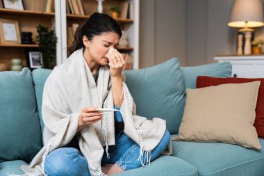 Hastalık mevsimsel virüs problemi konsepti. Kanepede elinde termometreyle yatan hasta bir kadın. Hasta kadın yüksek ateşle yatakta yatıyor. Soğuk algınlığı ve yüksek vücut sıcaklığında migren..