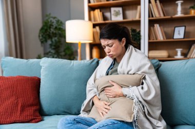 Regl olmuş genç bir kadın kanepeye uzanıyor ve karnına tutunuyor çünkü regl döneminin ortasında acı dolu bir yüz ifadesi ile acı çekiyor.