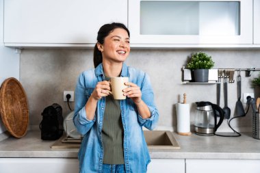 Young happy freshly divorced or recently single woman after toxic relationship breakup standing at kitchen in new apartment she rent drinking coffee or tea enjoying new beginnings and morning silence clipart