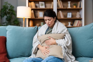 Karın ağrısı, kramplar ve karın ağrısı olan bir kadının elleri kabızlık, regl ya da klozet sorunu yüzünden ağrıyordu. Hasta, ev ve insan acı çekiyor ve karnını bir salonda, kanepede ve oturma odasında tutuyor.