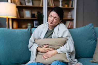 Karın ağrısı, kramplar ve karın ağrısı olan bir kadının elleri kabızlık, regl ya da klozet sorunu yüzünden ağrıyordu. Hasta, ev ve insan acı çekiyor ve karnını bir salonda, kanepede ve oturma odasında tutuyor.