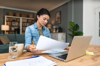 Ev ofisinde dizüstü bilgisayarla çalışan kendine güvenen genç bir iş kadını. İşletme sahibi profesyonel kadın, hesaplayan ve düşünen, e-ticaret alanında verilerle yenilikler yapan.