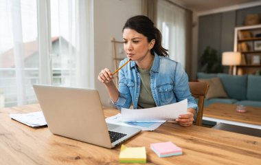 Ev ofisinde dizüstü bilgisayarla çalışan kendine güvenen genç bir iş kadını. İşletme sahibi profesyonel kadın, hesaplayan ve düşünen, e-ticaret alanında verilerle yenilikler yapan.