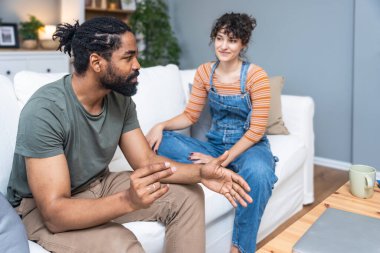 Smiling millennial couple sit on sofa in living room involved in interesting pleasant conversation at home, happy young man and woman talk chat relaxing on couch, enjoy romantic weekend or date