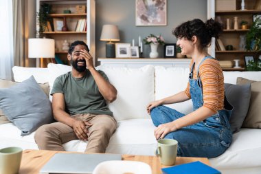 Smiling millennial couple sit on sofa in living room involved in interesting pleasant conversation at home, happy young man and woman talk chat relaxing on couch, enjoy romantic weekend or date