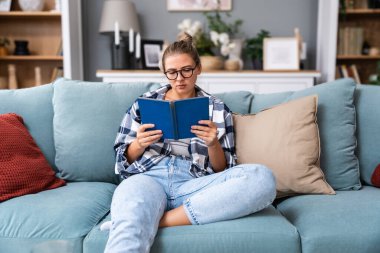 Açık kağıt tutan mutlu rahat genç kadın kitap zevk modern edebiyat Yeni kanepe evde, hafta sonu harcama bestseller ilginç genç hippi kız okuma roman kanepede oturan gülümseyen