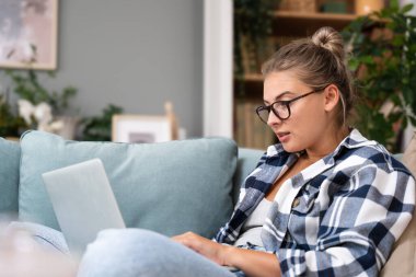 Tatmin olmuş bir kadın öğrenci evde dizüstü bilgisayar kullanıyor sosyal ağda arkadaşlarıyla sohbet ediyor tembelce hafta sonları film izliyor, internetten alışveriş yapıyor, e-posta yazıyor..