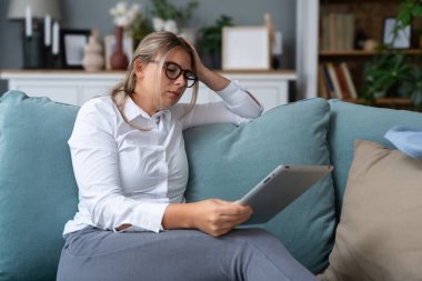 Çekici bir kadın, serbest çalışan, dijital tablet kullanan, oturma odasında rahat bir koltukta oturan. Başarılı bir iş kadını evde mesaj atıyor. Çevrimiçi teknoloji kavramı, uzak meslek.