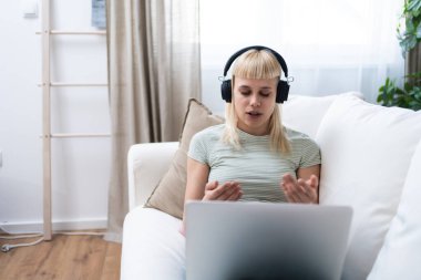 Genç ve güzel bir iş kadını kanepeye uzanmış ev ofisinin bilgisayarını kullanıyor, internette çalışıyor, e-ticaret, online kurs ve eğitim için video çağrısı alıyor, e-öğrenme, iş rutini.