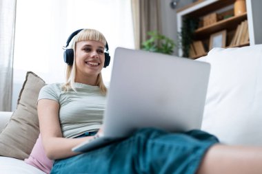 Genç ve güzel bir iş kadını kanepeye uzanmış ev ofisinin bilgisayarını kullanıyor, internette çalışıyor, e-ticaret, online kurs ve eğitim için video çağrısı alıyor, e-öğrenme, iş rutini.