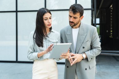 Modern ofis binasının dışında duran iki iş adamı, yeni proje üzerinde çalışan dijital tablet kullanıyorlar iş konularını tartışıyor ve açıklıyorlar ve gülümsüyorlar. Profesyonel işgalci kişiler tasarla