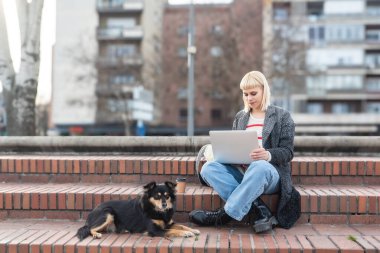 Profesyonel tasarım. Serbest çalışan genç bir iş kadını, bilgisayar yazılımı geliştiricisi, web tasarımcısı, evcil köpeği ve dizüstü bilgisayarıyla dışarıda otururken uzaktan çalışıyor..