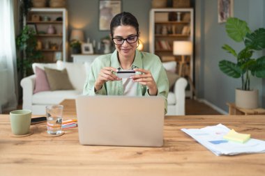 Serbest çalışan genç bir iş kadını, evde çalışıyor, işe ara veriyor, kredi kartını online alışveriş ve alım için kullanıyor. Happy, internete para harcıyorsun..