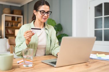 Serbest çalışan genç bir iş kadını, evde çalışıyor, işe ara veriyor, kredi kartını online alışveriş ve alım için kullanıyor. Happy, internete para harcıyorsun..