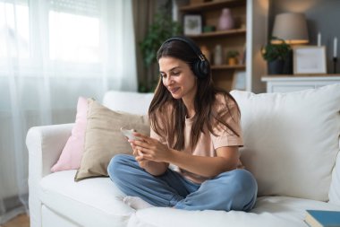 Kendini sevme zamanı. Genç ve güzel bir kadın küçük evinde dinleniyor ve dinleniyor modern stüdyo dairesinde, kablosuz kulaklıklarıyla müzik dinliyor, kanepede otururken. Hafta sonu aktiviteleri.