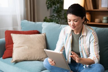 Çekici kadın, serbest çalışan, dijital tablet kullanan, oturma odasındaki rahat koltukta oturan. Başarılı bir iş kadını evde mesaj atıyor. Çevrimiçi teknoloji konsepti, uzak meslek.