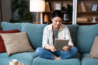 Çekici kadın, serbest çalışan, dijital tablet kullanan, oturma odasındaki rahat koltukta oturan. Başarılı bir iş kadını evde mesaj atıyor. Çevrimiçi teknoloji konsepti, uzak meslek.