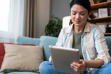 Çekici kadın, serbest çalışan, dijital tablet kullanan, oturma odasındaki rahat koltukta oturan. Başarılı bir iş kadını evde mesaj atıyor. Çevrimiçi teknoloji konsepti, uzak meslek.