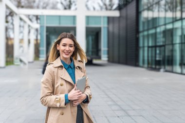 Ofis binasının önünde dijital tablet kullanarak şık kıyafetler giyen başarılı genç bir iş kadınının portresi. Profesyonel meslek kadını, ofisten personel toplantısına yürürken çalışıyor.