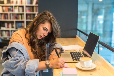 Serbest çalışan genç bir iş kadını, çalışmaktan yorgun ve yorgun, kütüphanede dizüstü bilgisayarla tembel tembel çalışıyor. Stresli ve endişeli kadın yeni projede beyin fırtınası yapıyor. Yenilikçi fikirler.