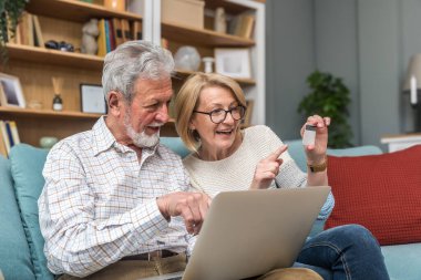 Üst düzey çift, erkek ve kadın, online alışveriş ve sipariş için dizüstü bilgisayar ve banka kredi kartı kullanıyorlar. Evdeki kanepede otururken internet ve teknoloji kullanan evli insanlar..