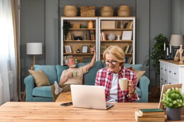 70 'lerin çifti kanepeye dizüstü bilgisayarlı internet sitesi ve banka kredi kartı rezervasyonlu otel planı tatili ile oturur, yaşlı çiftler internet konseptinde hizmet veya ürün seçerek ödeme sistemini öğrenirler.