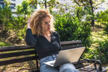 Parktaki bankta oturan genç bir üniversite öğrencisi dizüstü bilgisayarda ders çalışıyor ve okuyor. Üniversitede final sınavına hazırlanıyor. Aygıttaki e- postalar kontrol ediliyor, sınıf çizelgesi.