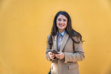 Başarılı bir iş kadınının portresi, resmi kıyafetler içinde sarı ya da turuncu duvarın önünde duran bir ofis çalışanı. Güçlü bağımsız profesyonel işgal kadın lider pozu.