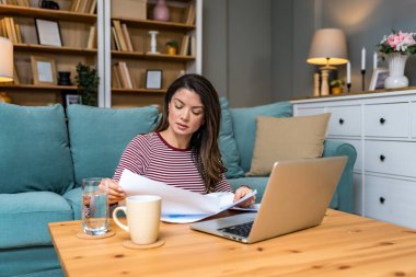 Finansal kriz. Genç endişeli iş kadını evde oturmuş, istatistik ve dizüstü bilgisayar kullanarak küçük küresel işletme şirketinin gelir ve giderlerini hesaplamaya çalışıyor..