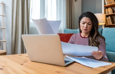 Finansal kriz. Genç endişeli iş kadını evde oturmuş, istatistik ve dizüstü bilgisayar kullanarak küçük küresel işletme şirketinin gelir ve giderlerini hesaplamaya çalışıyor..