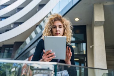 Genç iş kadını güneşli bir günde dijital tablet kullanıyor, şehir parkında uzaktan çalışıyor, Modern Teknoloji ve Esnek Çalışmaları Gündelik ama Profesyonel Ayarlarda Kucaklıyor.