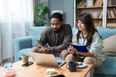 Genç, zeki, yenilikçi bir çift yeni iş fikirlerini dizüstü bilgisayarla sunuyorlar. Evde kanepede oturup potansiyel yatırımcılarla konuşuyorlar. Teknoloji yeniliği.