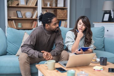 Genç, zeki, yenilikçi bir çift yeni iş fikirlerini dizüstü bilgisayarla sunuyorlar. Evde kanepede oturup potansiyel yatırımcılarla konuşuyorlar. Teknoloji yeniliği.