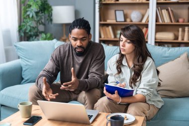 Genç, zeki, yenilikçi bir çift yeni iş fikirlerini dizüstü bilgisayarla sunuyorlar. Evde kanepede oturup potansiyel yatırımcılarla konuşuyorlar. Teknoloji yeniliği.