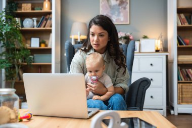 Genç, zeki, yenilikçi bekar anne dizüstü bilgisayarla yeni iş fikrini sunuyor, evde bebekle oturuyor, potansiyel yatırımcıyla konuşuyor. Teknoloji yeniliği.