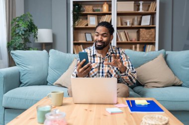 Genç serbest çalışan bir iş adamı dizüstü bilgisayarında video konferansı düzenlerken evde oturuyor ve projesinde potansiyel yatırımcıyla web kamerasında konuşuyor. Maliye ve ekonomi kavramı.