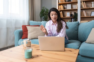 Genç serbest çalışan bir iş kadını dizüstü bilgisayarında video konferansına katılıyor ve evde çalışıyor, projesinde potansiyel yatırımcıyla web kamerasında konuşuyor. Maliye ve ekonomi kavramı.