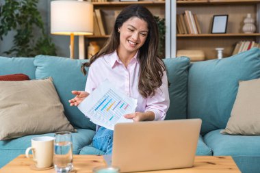 Genç serbest çalışan bir iş kadını dizüstü bilgisayarında video konferansına katılıyor ve evde çalışıyor, projesinde potansiyel yatırımcıyla web kamerasında konuşuyor. Maliye ve ekonomi kavramı.