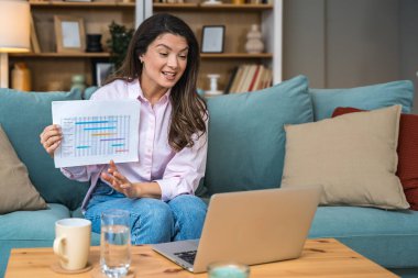 Genç serbest çalışan bir iş kadını dizüstü bilgisayarında video konferansına katılıyor ve evde çalışıyor, projesinde potansiyel yatırımcıyla web kamerasında konuşuyor. Maliye ve ekonomi kavramı.