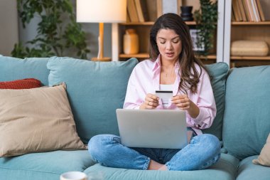 Tüketim ve alışveriş düşkünlüğü. Genç bir kadın kanepesinde oturuyor ve ihtiyacı olmayan şeyleri internetten almak için banka kartı kullanıyor. Alışverişe bağımlı, aşırı harcamaya. Zihinsel bağımlılık.