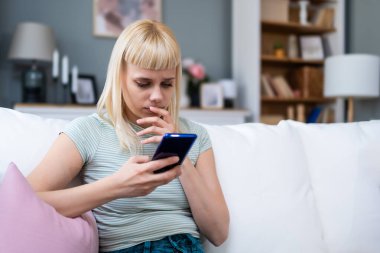 Genç bir kadın rahat koltukta tek başına rahat bir şekilde rahat bir şekilde rahat rahat rahat oturup mesajlaşmak, yayın yapmak, alışveriş yapmak, video sohbeti yapmak, okumak, göz atmak, oyun oynamak, uzaktan çalışmak, bankacılık, öğrenmek, programlamak için akıllı telefon kullanıyor..