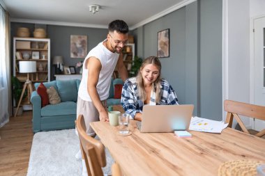 Genç çift evlerinde uzaktan çalışıyor, belge ve verileri analiz ediyor, rahat modern oturma odasında dizüstü bilgisayar kullanıyor, mali raporları ve iş stratejisini tartışıyor. Birkaç hedef, basit yaşam desteği..
