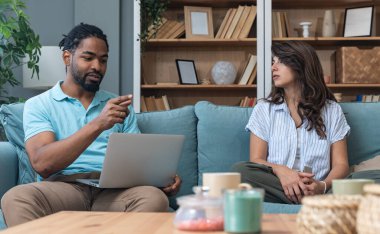 Genç çift evlerinde uzaktan çalışıyor, belge ve verileri analiz ediyor, rahat modern oturma odasında dizüstü bilgisayar kullanıyor, mali raporları ve iş stratejisini tartışıyor. Birkaç hedef, basit yaşam desteği..