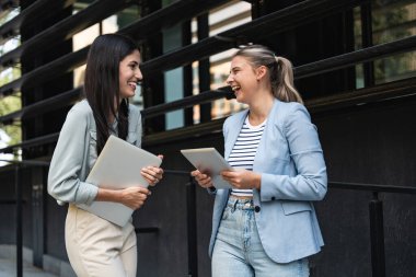 Kurumsal profesyonellerden oluşan çeşitli bir ekip dışarıda iş birliği yapıyor, modern cam ofis binası önünde dizüstü bilgisayardaki verileri analiz ederken stratejik tartışmalara girişiyorlar..