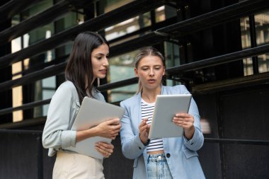 Kurumsal profesyonellerden oluşan çeşitli bir ekip dışarıda iş birliği yapıyor, modern cam ofis binası önünde dizüstü bilgisayardaki verileri analiz ederken stratejik tartışmalara girişiyorlar..